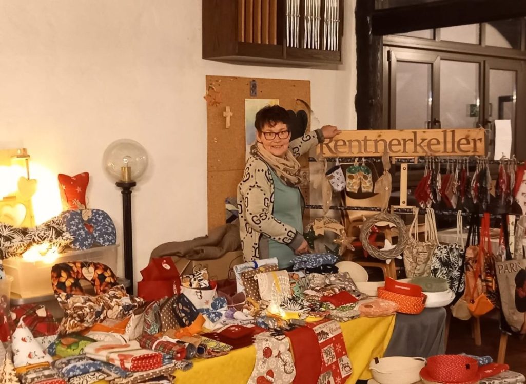 Frau neben einem bunten Stand mit handgemachten Produkten und Dekorationen.
