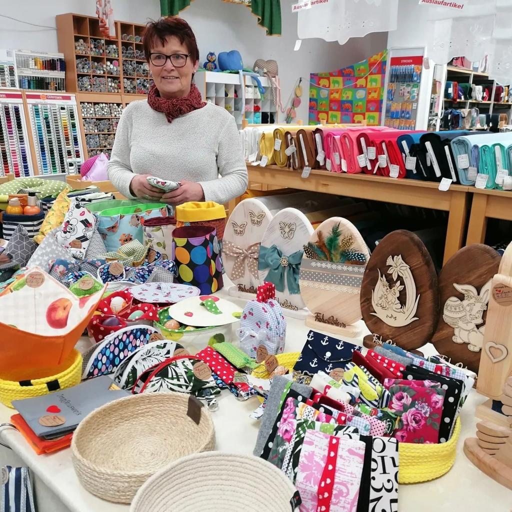 Eine Frau steht an einem Tisch voller handgefertigter Bastelmaterialien und Dekorationen.