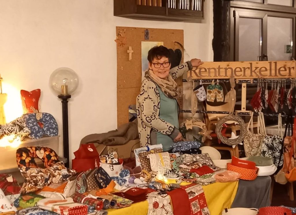 Frau neben einem bunten Stand mit handgemachten Produkten und Dekorationen.